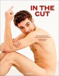Nude white male, sitting floor, smiling at camera, holding middle finger in air, white cover, IN THE CUT in red font to upper right.
