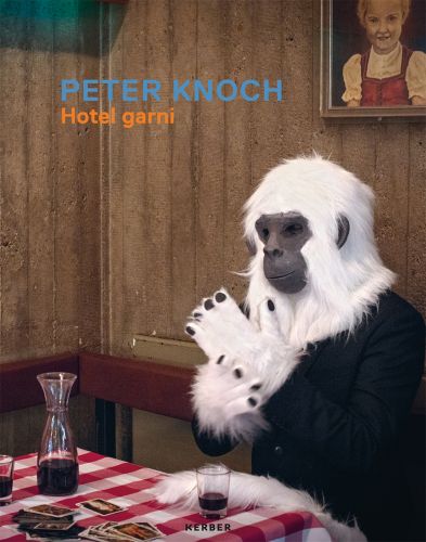 Figure wearing furry white monkey suit, sitting at café table, decanter of red wine with glass, PETER KNOCH Hotel garni in blue and orange font above.