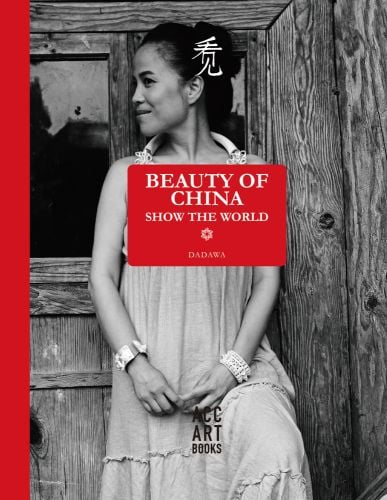 Black and white three quarter length photograph of Zhu Zheqin in a long dress with her face turned to her right standing in front of a wooden door with Beauty of China Show the World DADAWA in white on a red rectangle shape