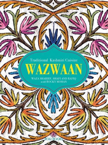 Decorative embroidered table cloth with pink and orange flowers, WAZWAAN in yellow font on green shape to centre.