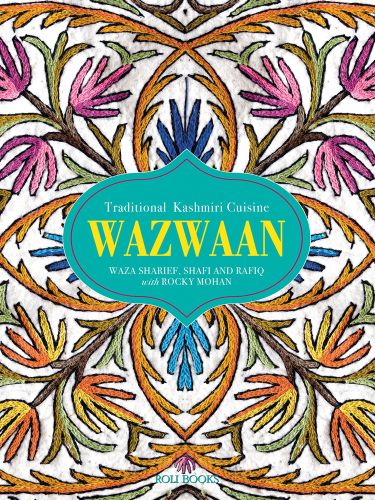 Decorative embroidered table cloth with pink and orange flowers, WAZWAAN in yellow font on green shape to centre.