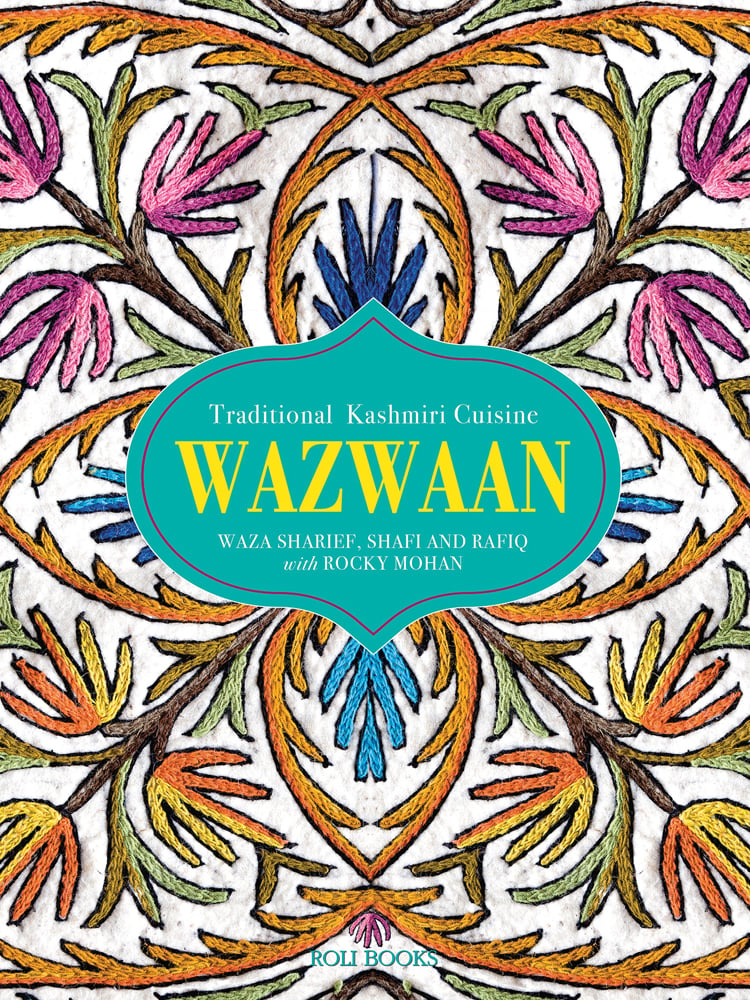 Decorative embroidered table cloth with pink and orange flowers, WAZWAAN in yellow font on green shape to centre.