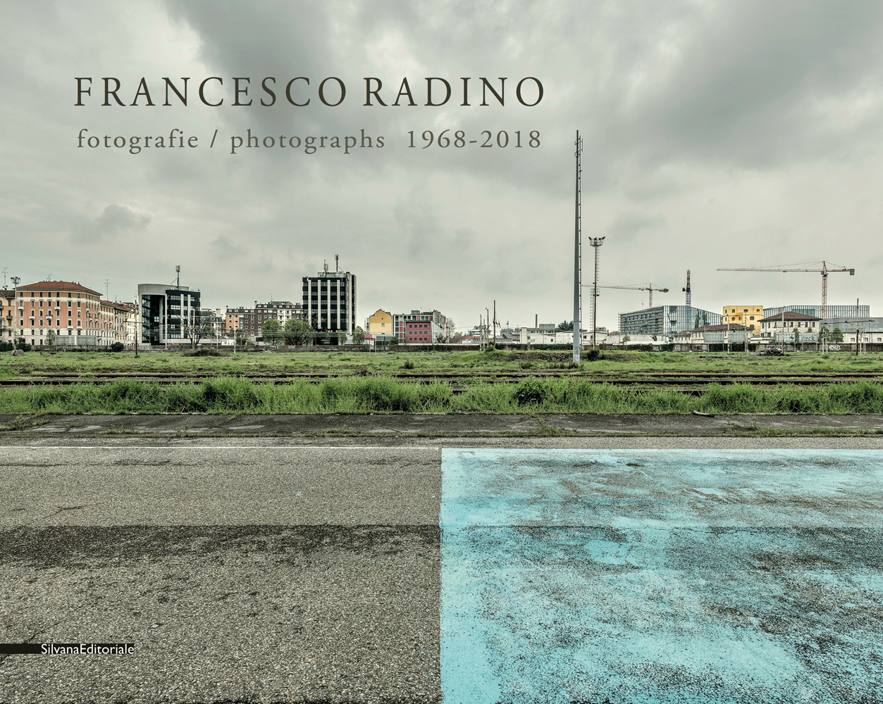 Urban landscape with road, train track, high rise buildings and machine cranes, FRANCESCO RADINO fotographie/photographs 1968-2018 in green font above.