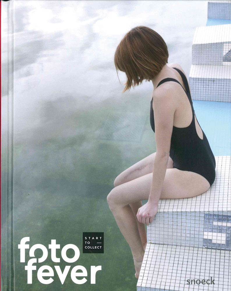 Full length photograph of female in black bathing suit sitting on edge of sheer drop, white tiled surface, fotofever in white font to bottom left.