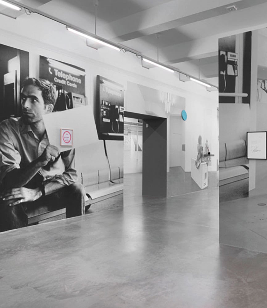 Exhibition interior space with large photographic portrait of seated man holding a sheet of paper.