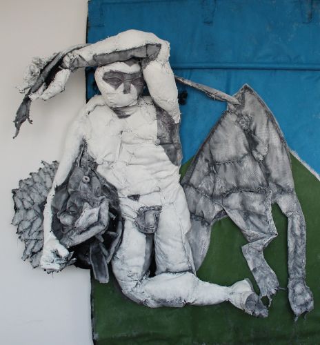 Fabric sculpture of nude male figure slumped on blue and green fabric landscape