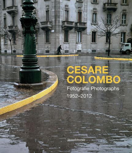 Shot of wet brick roads of Milan in rain, surrounded by buildings, CESARE COLOMBO Fotographie Photographs 1952-2012 in yellow and white font to centre right.
