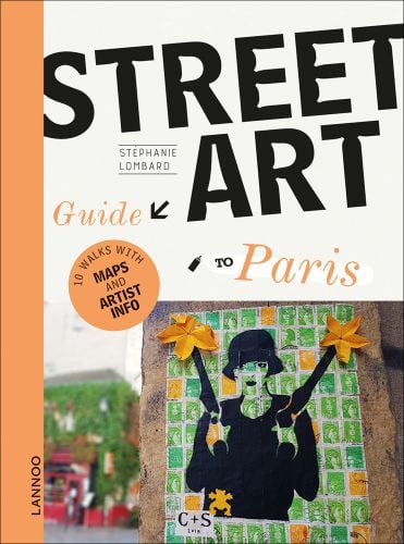 Black graffiti stencil of female in bowler hat holding 2 guns, 2 yellow flowers on barrels, green and yellow stamps behind, on brick wall, STREET ART Guide TO Paris in black and pale orange font above.