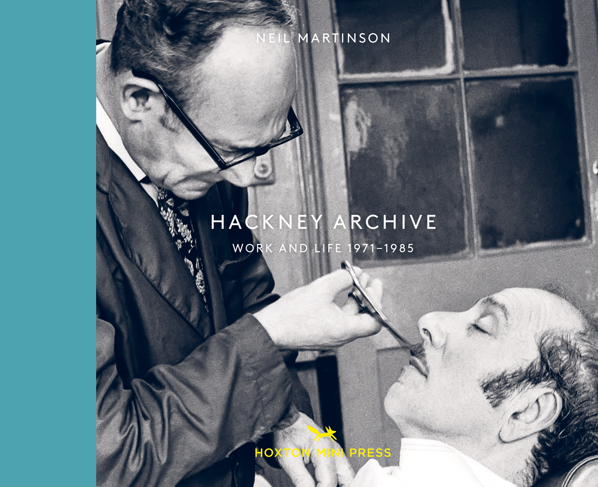 Barber using pair of scissors to cut white man's moustache as he sits back in chair, on landscape cover of 'Hackney Archive, Work and Life 1971-1985', by Hoxton Mini Press.