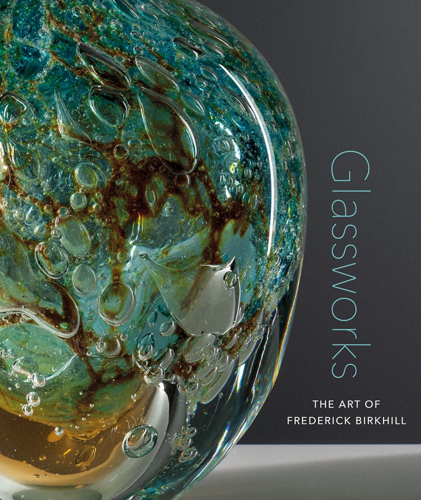 Large rounded glass artwork in turquoise and amber, with air bubbles beneath surface, grey cover, Glassworks THE ART OF FREDERICK BIRKHILL in turquoise and white font to lower right.
