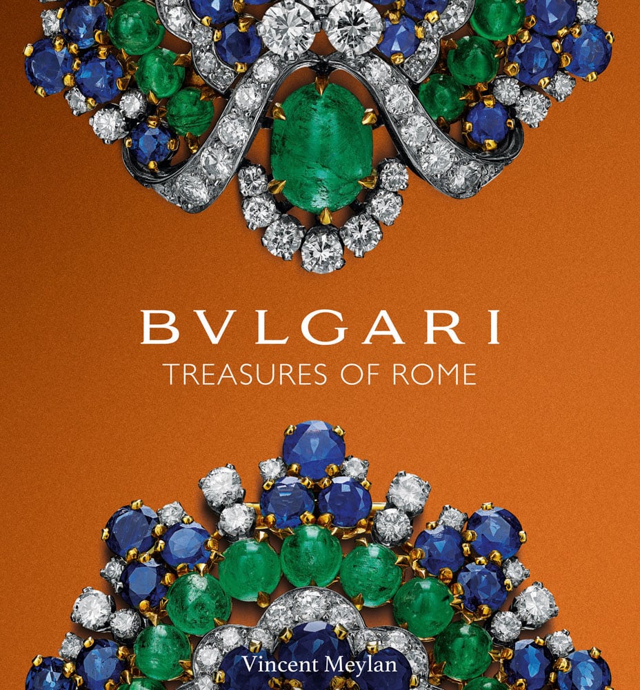 Two halves of luxury blue and green gemstone encrusted jewellery on an orange background with Bulgari Treasures of Rome in white font in centre