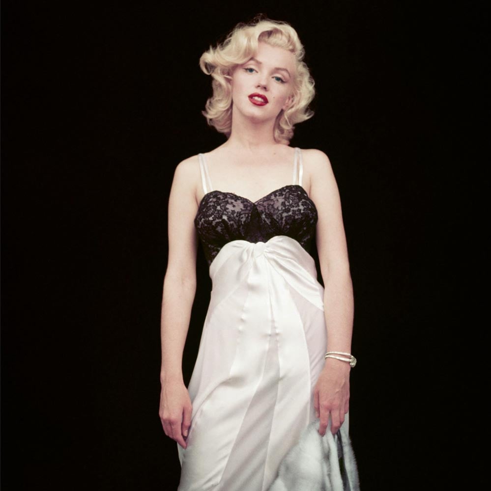 Relaxed pose of Marilyn Monroe gazing into camera wearing black and white skirt and bodice on black cover.