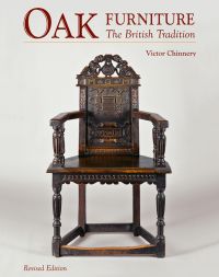 Large dark oak chair with carved back panel, on white cover of 'Oak Furniture', by ACC Art Books.