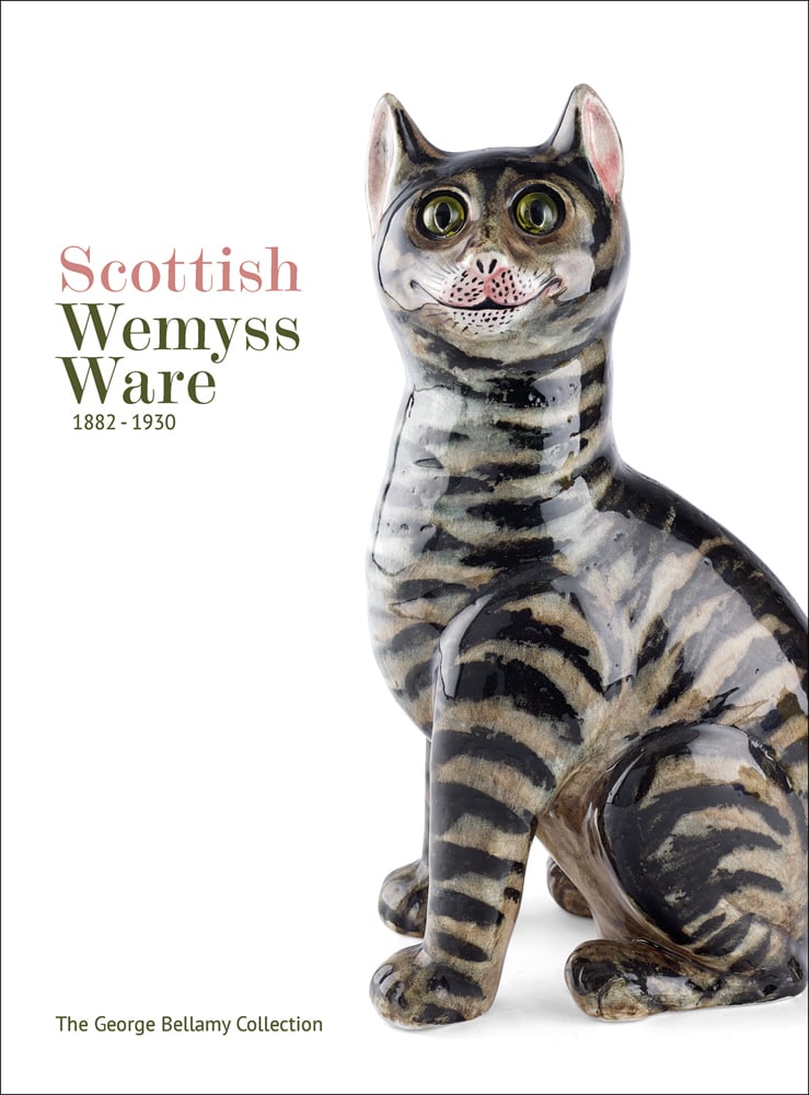 White cover with a comical ceramic glazed cat smiling with large green eyes and Scottish Wemyss Ware 1882-1930 in pink and green font