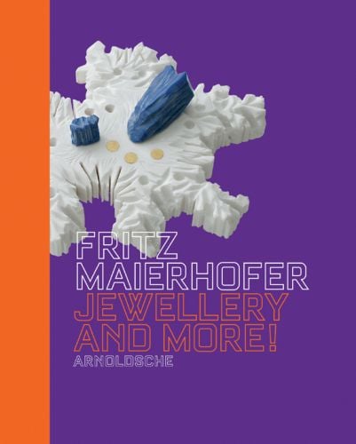 White plastic jagged shape with blue pieces and three gold dots, on purple cover of 'Fritz Maierhofer, Jewellery and More!', by Arnoldsche Art Publishers.