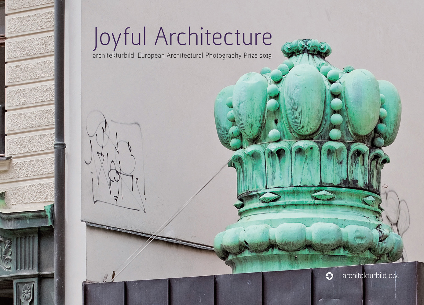 Mint green crown shaped structure tied down with rope, next to street building, on landscape cover of 'Joyful Architecture, European Architectural Photography Prize 2019', by Avedition Gmbh.