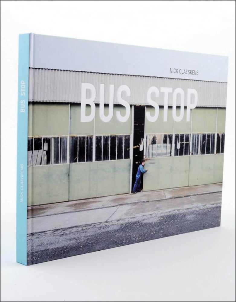 Man in overalls pushing open door of run down bus depot with Nick Claeskens BUS STOP in black and white font