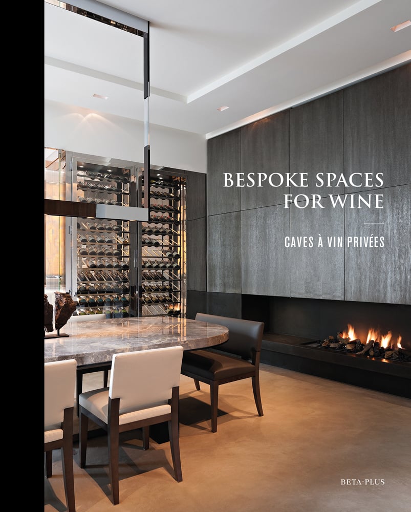 Minimalist interior, marble table, tall wine rack unit, lit fireplace, on cover of 'Bespoke Spaces for Wine', by Beta-Plus.