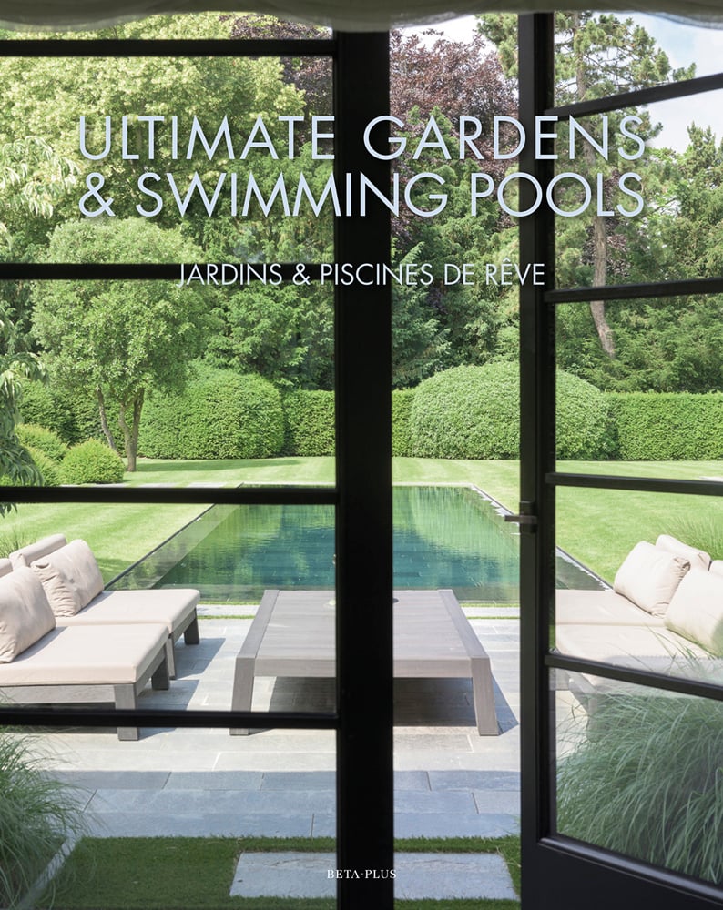 Swimming pool in landscaped garden through interior glass doors, table and chairs on patio, on cover of 'Ultimate Gardens & Swimming Pools', by Beta-Plus.