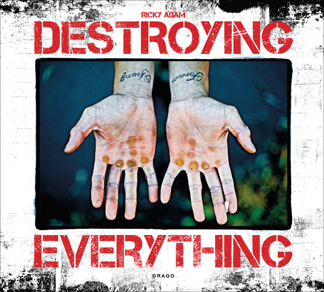 Open pair of hands with blisters to palms, script tattoos on wrists, on white cover of 'Destroying Everything...Seems Like the Only Option', by Drago.