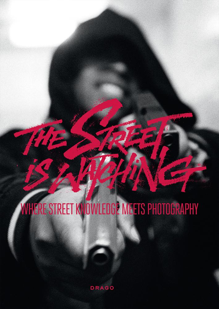 Figure with hood pointing gun a the camera, on cover of 'The Street Is Watching, Where Street Knowledge Meets Photography', by Drago.