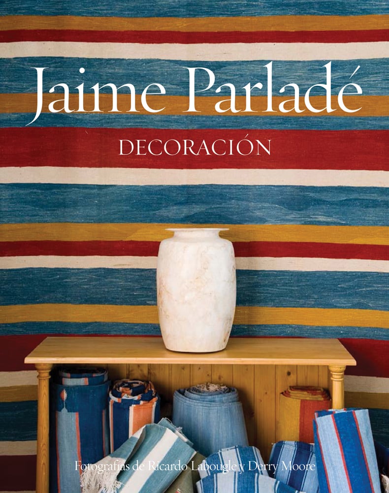 Open wood cabinet with white vase on top, rolls of striped material inside, striped material behind, on cover of 'Jaime Parlade', by Ediciones El Viso.