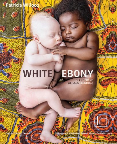 Two naked babies sleeping side by side: one albino baby, one black baby, on colourful sheet, on cover of 'White Ebony', by Edition Lammerhuber.