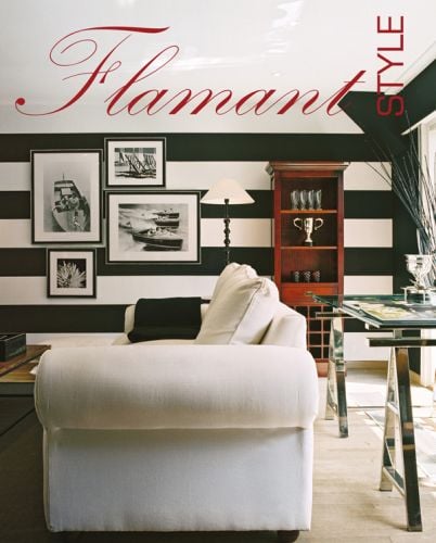 Interior living room with large soft white sofa, black and white striped wallpaper, and framed photography, on cover of 'Flamant Style', by Lannoo Publishers.