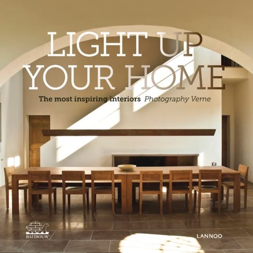 Interior dining room with long wood table and chairs through hall arch, on cover of 'Light Up Your Home, The Most Inspiring Interiors', by Lannoo Publishers.