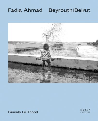 Small child facing sea waves crashing into low wall on pale blue cover, of 'Fadia Ahmad. Beyrouth | Beirut', by Editions Norma.