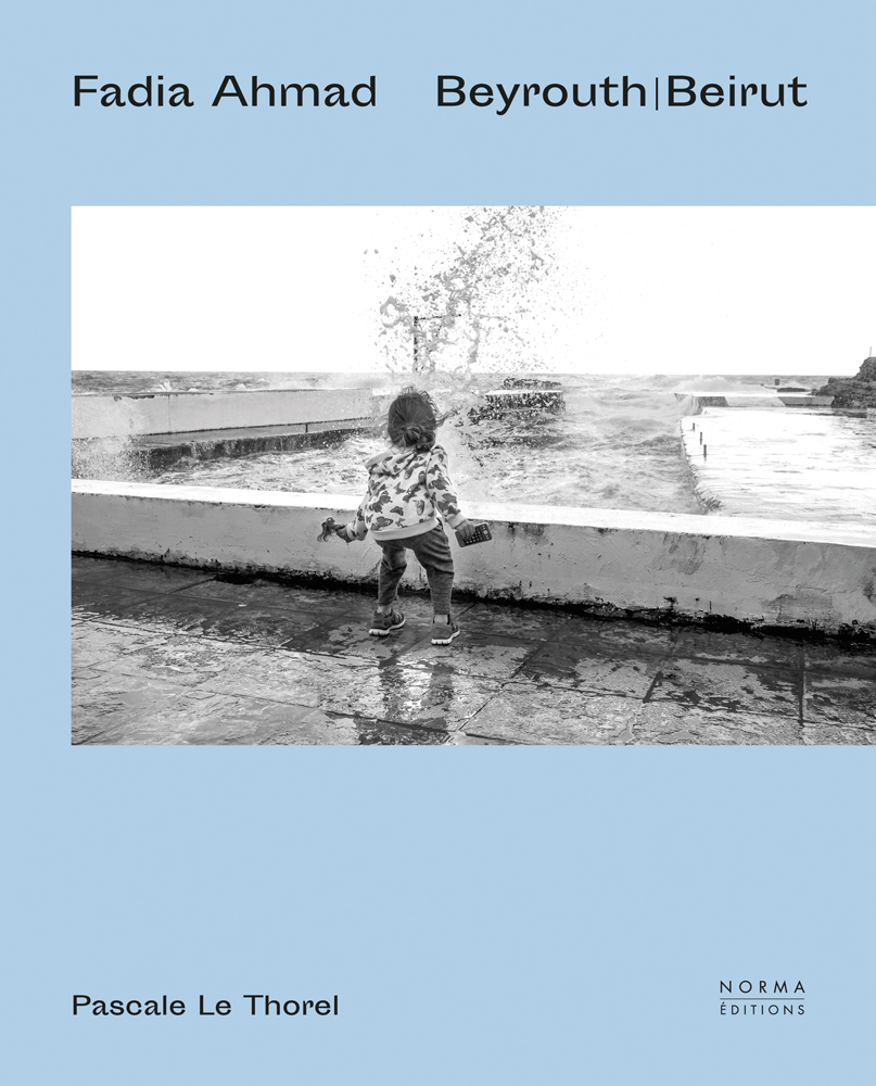 Small child facing sea waves crashing into low wall on pale blue cover, of 'Fadia Ahmad. Beyrouth | Beirut', by Editions Norma.