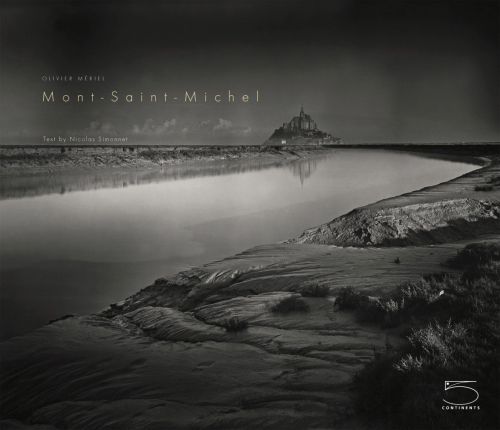 Atmospheric black and white shot of Mont-Saint-Michel, under black sky, Mont-Saint-Michel in cream font to upper left.