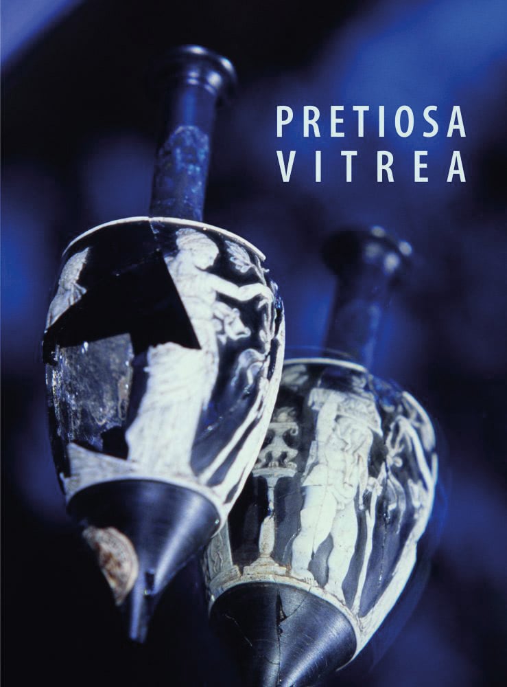 2 Navy and cream glass long necked vessels, on blue cover, PRETIOSA VITREA in white font to upper right.