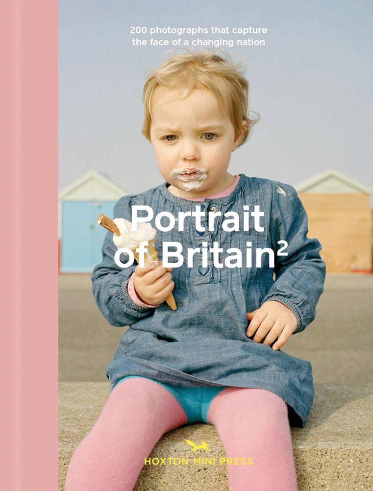 Young white child in blue denim dress, sitting on sea wall, holding dripping ice-cream cone, on landscape cover of 'Portrait of Britain 2, 200 Photographs that Capture the Face of a Changing Nation', by Hoxton Mini Press.