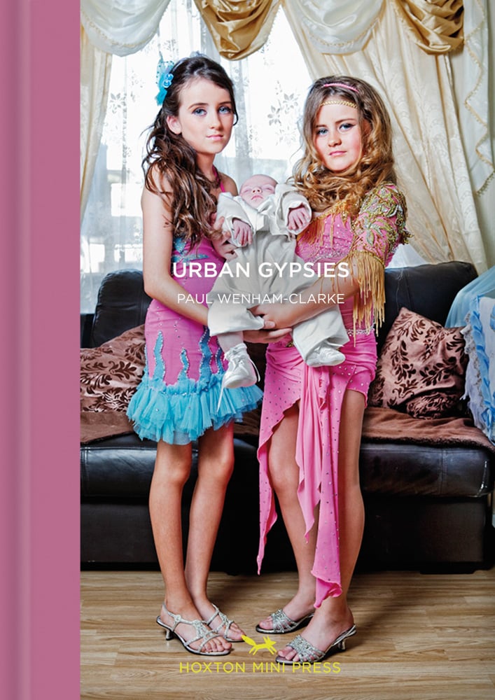 Two young white female travelers in pink and blue sparkly dresses, holding a sleeping baby, on cover of 'Urban Gypsies', by Hoxton Mini Press.