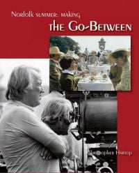 Book cover of Christopher Hartop's Norfolk Summer: Making The Go-Between, with two directors standing behind a large camera, and a scene still of a family sitting at a table. Published by John Adamson.