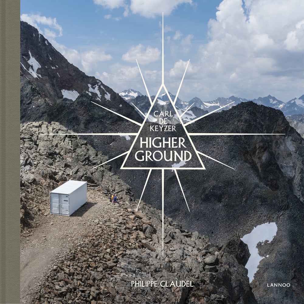 Aerial view of mountain range, snowy peaks in distance, shipping container sitting on dead-end road, on cover of 'Higher Ground', by Lannoo Publishers.