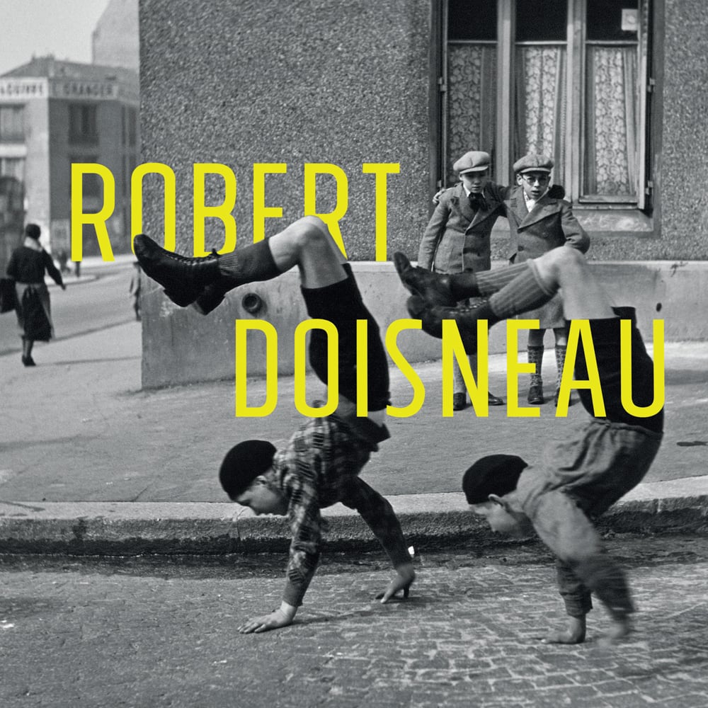 Two boys walking on hands on cobbled street in Victorian dress, on cover of 'Robert Doisneau', by Lannoo Publishers.