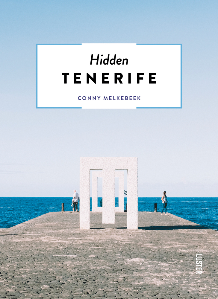 White pillared structures on cobbled surface, blue sea behind, Hidden Tenerife in black font on white banner above