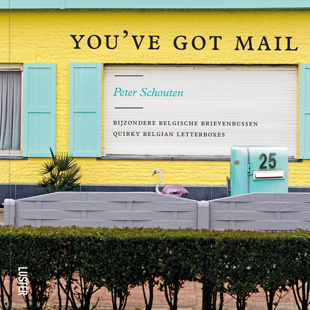Pale turquoise mail box, 25 on front, yellow building behind, row of hedging to front, YOU'VE GOT MAIL in black font above.