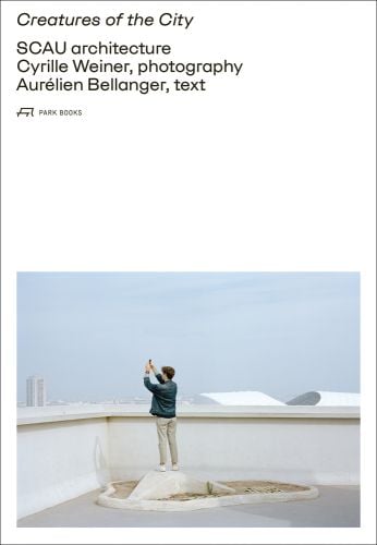 Man on white plinth taking photo of landscape, on white cover, Creatures of the City in black font above