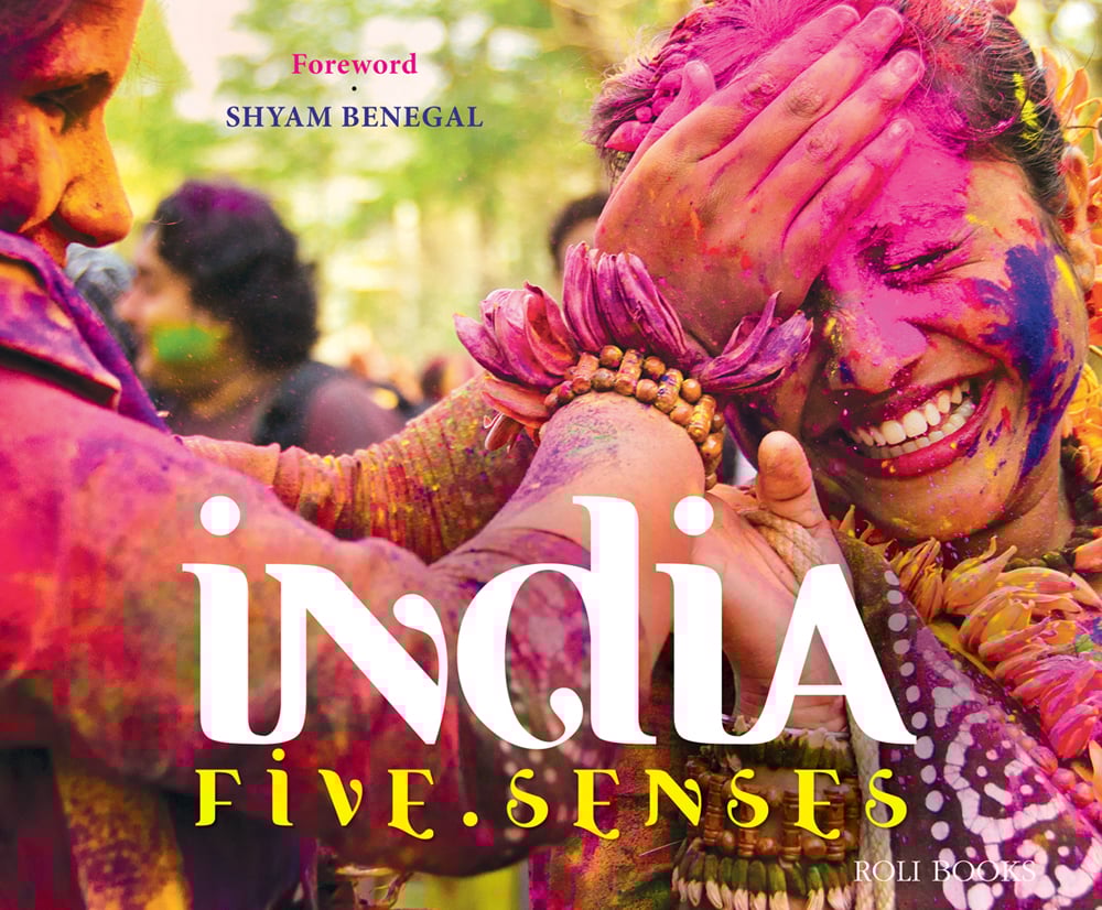Book cover of India 5 Senses, featuring festival goers covered in colorful paint, celebrating Holi. Published by Roli Books.