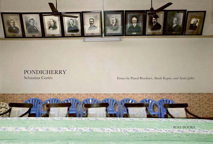 Book cover of Pondicherry, featuring a room with a long table, and old portrait photographs behind. Published by Roli Books.
