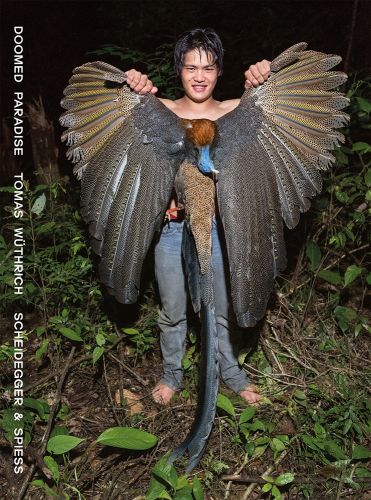 Indigenous male holding a dead great argus pheasant at night in Bornea rainforest, DOOMED PARADISE in white font down left edge.