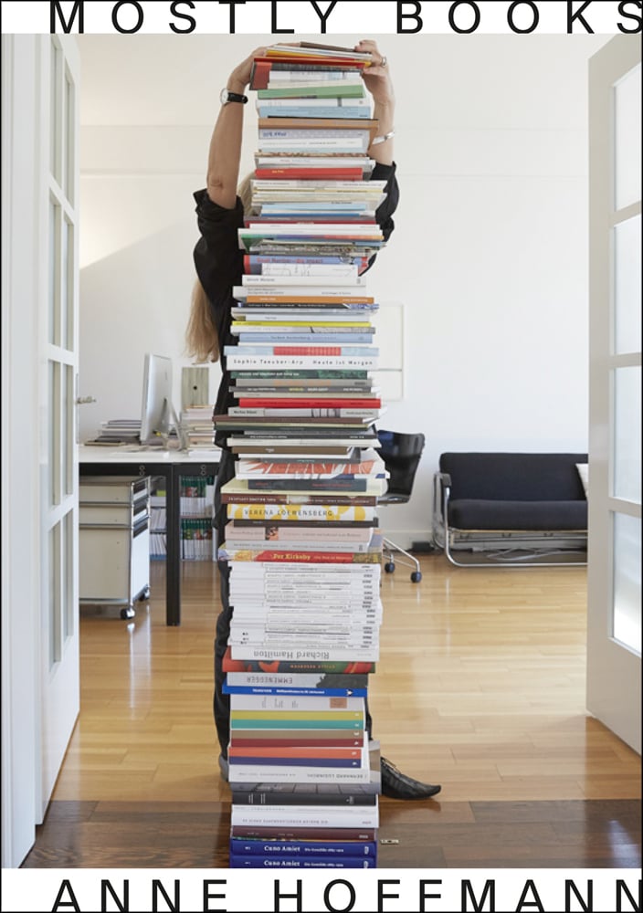 Stack of books with standing figure behind, Mostly Books Anne Hoffman in black font on white cover