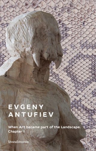 Carved wood breasted figure with large fanged skull on head, beige snake skin cover, EVGENY ANTUFIEV in white font to lower left