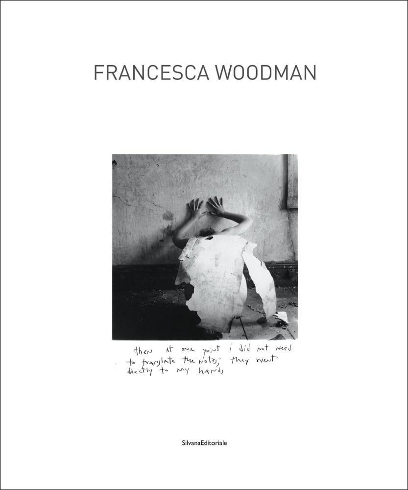 Portrait of figure crouched down, hands to wall, torn white paper over back, on white cover, FRANCESCA WOODMAN in grey font above