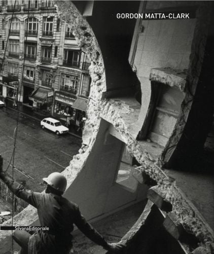 Concrete building with circular piece cut out to front, exposing street below, hardhat worker, GORDON MATTA-CLARK in white font to upper right