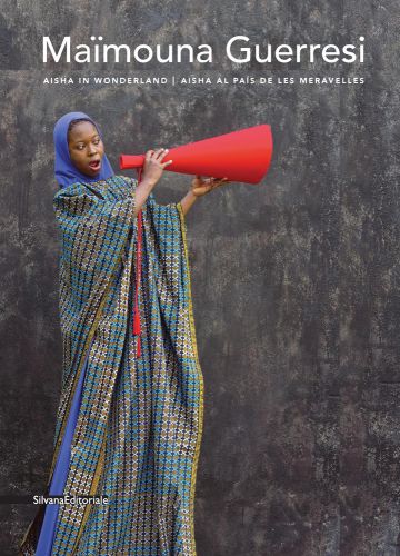 African woman in blue and mustard decorative hooded dress, shouting through red megaphone, Maimouna Guerresi in white font above.