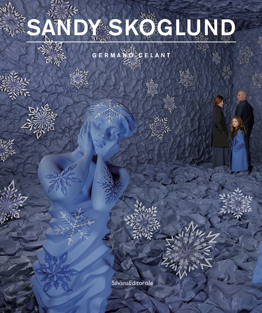 3 figures huddled in corner of blue fabric covered room, blue sculpture in foreground, white snowflakes, SANDY SKOGLUND in white font above
